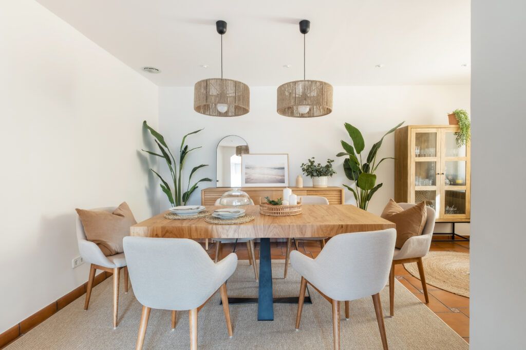 Comedor luminoso con mesa de madera, lámparas de fibras naturales y plantas que muestra cómo transformar el espacio sin reformar mediante decoración y materiales cálidos.