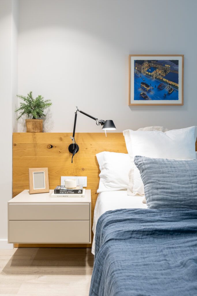 Dormitorio con cabecero de madera natural y lámpara de pared que muestra cómo transformar el espacio sin reformar mediante iluminación y materiales cálidos.