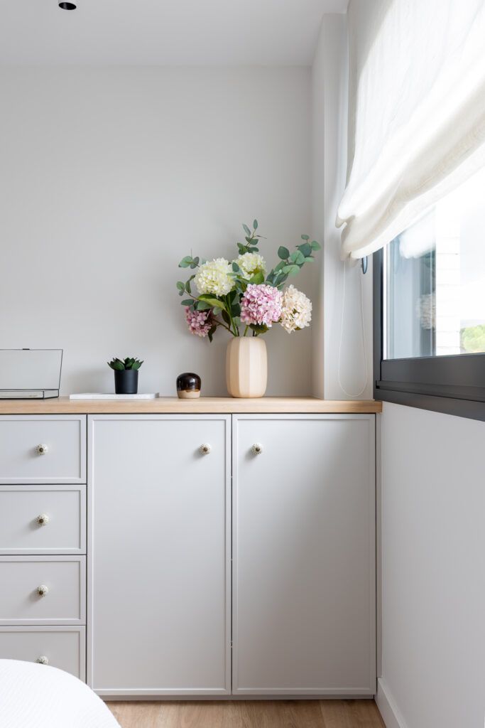 Cómoda blanca junto a una ventana con luz natural y jarrón decorativo que muestra cómo transformar el espacio sin reformar mediante orden y pequeños detalles.