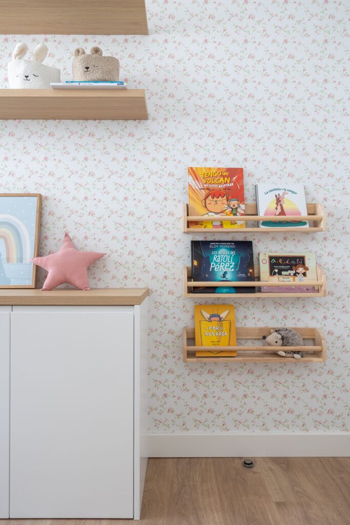 Dormitorio infantil con papel pintado floral y estanterías de madera que muestra cómo transformar el espacio sin reformar mediante color y almacenaje decorativo.