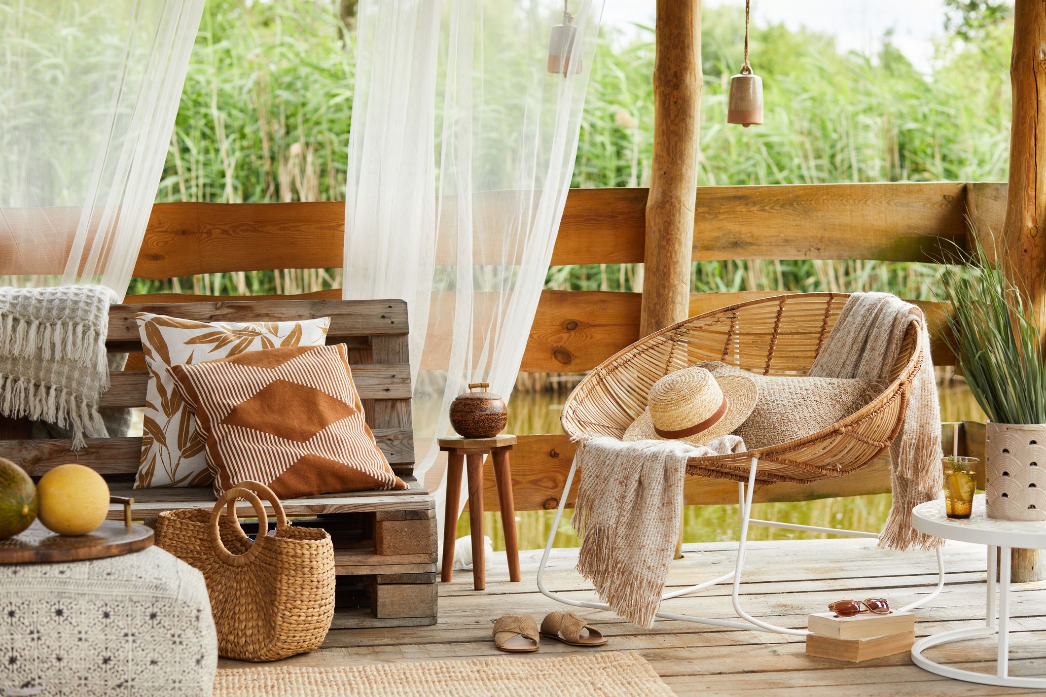 Terraza estilo chill out con sillón de ratán, cojines, manta y accesorios decorativos sobre suelo de madera