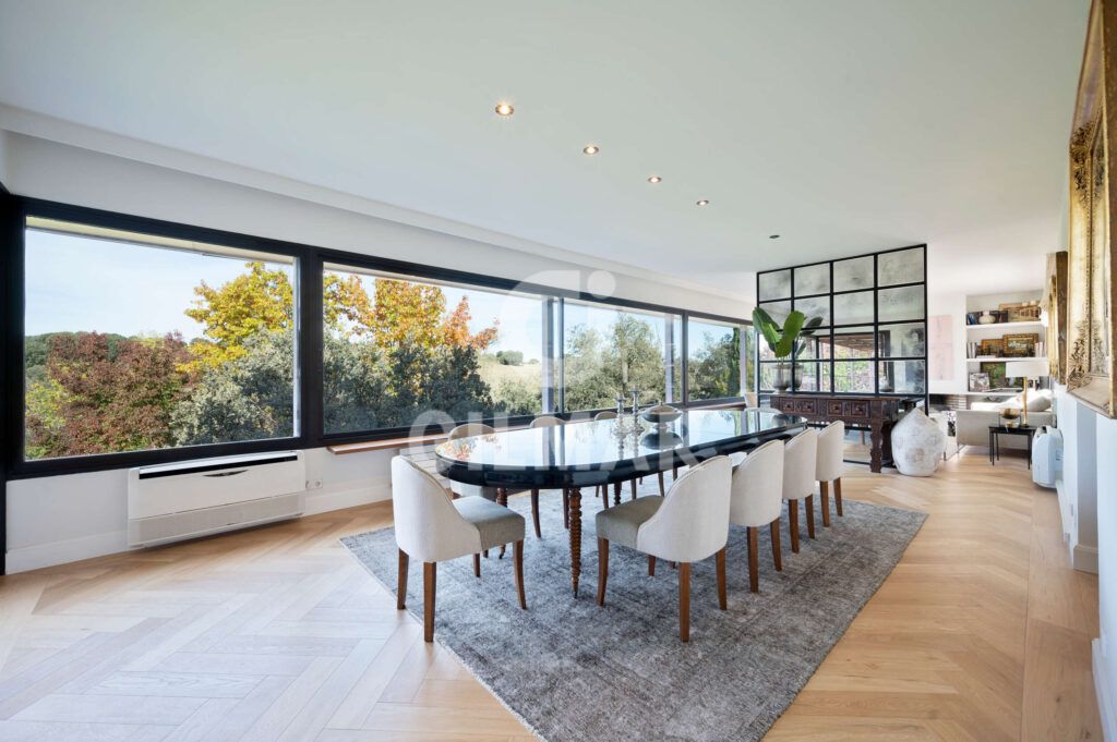 Comedor panorámico con mesa para ocho personas y grandes ventanales en un chalet en Madrid situado en Ciudalcampo.