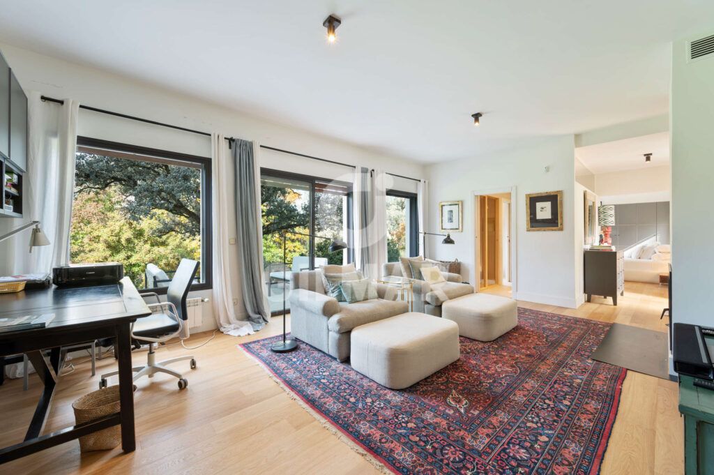 Salón con zona de trabajo y grandes ventanales en un chalet en Madrid situado en Ciudalcampo.