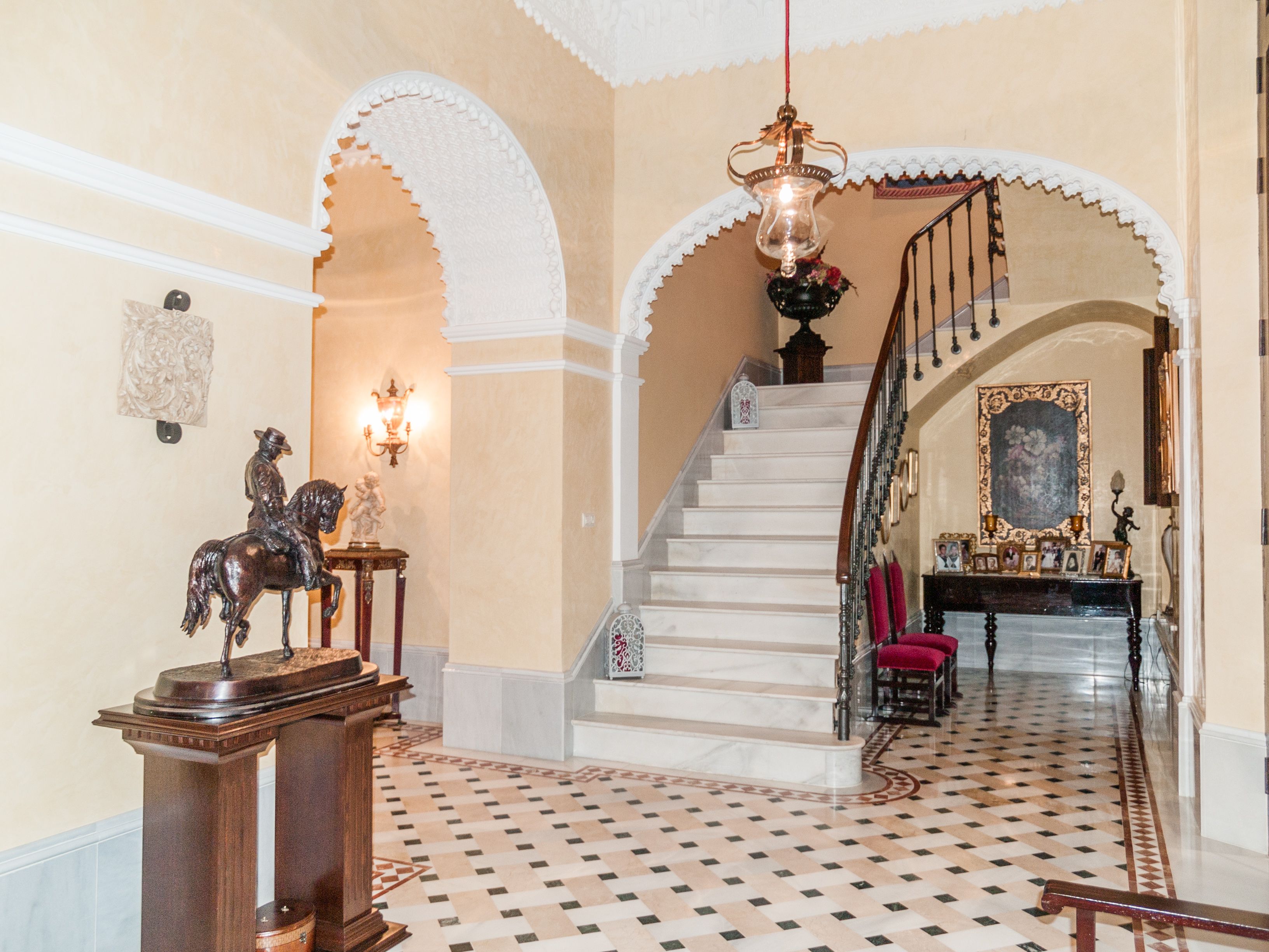 Hall de entrada de casa de lujo en Huelva con escalera curva, arcos decorativos y suelo hidráulico
