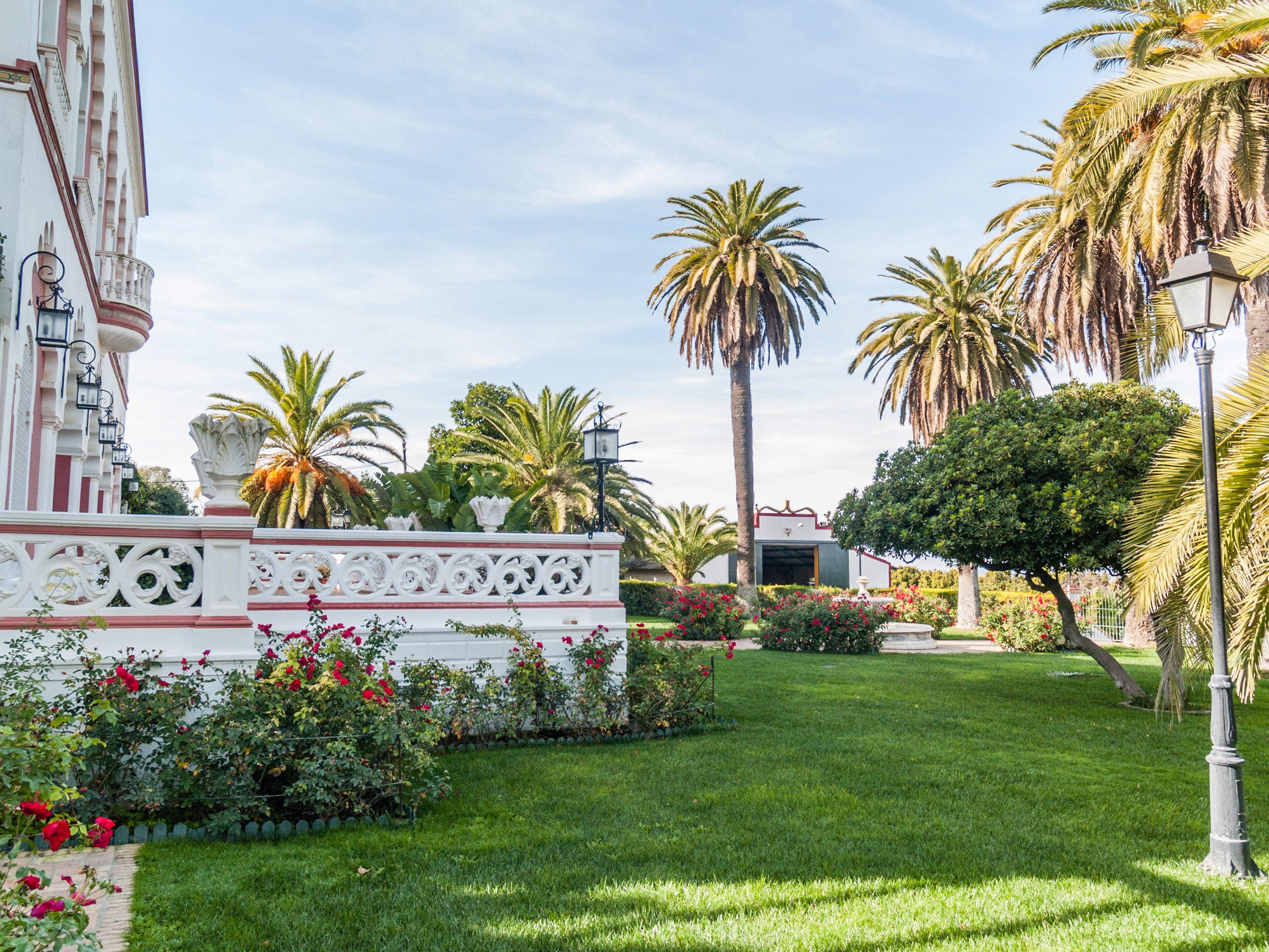 Jardín de casa de lujo en Huelva con palmeras, rosales y zonas verdes cuidadas
