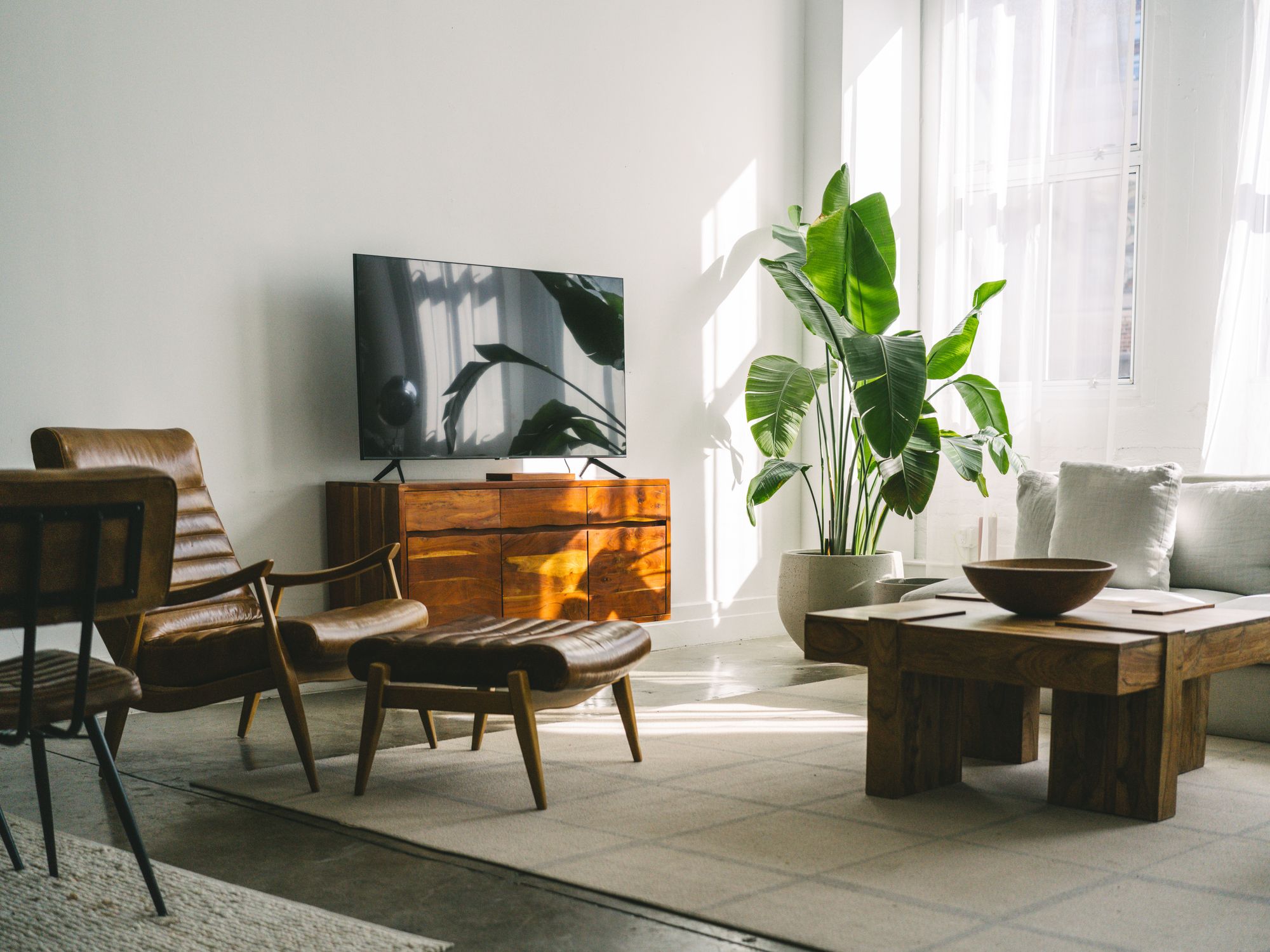Salón inspirado en el loft de Love Story con muebles de madera natural, sillón de cuero, textiles neutros y luz natural