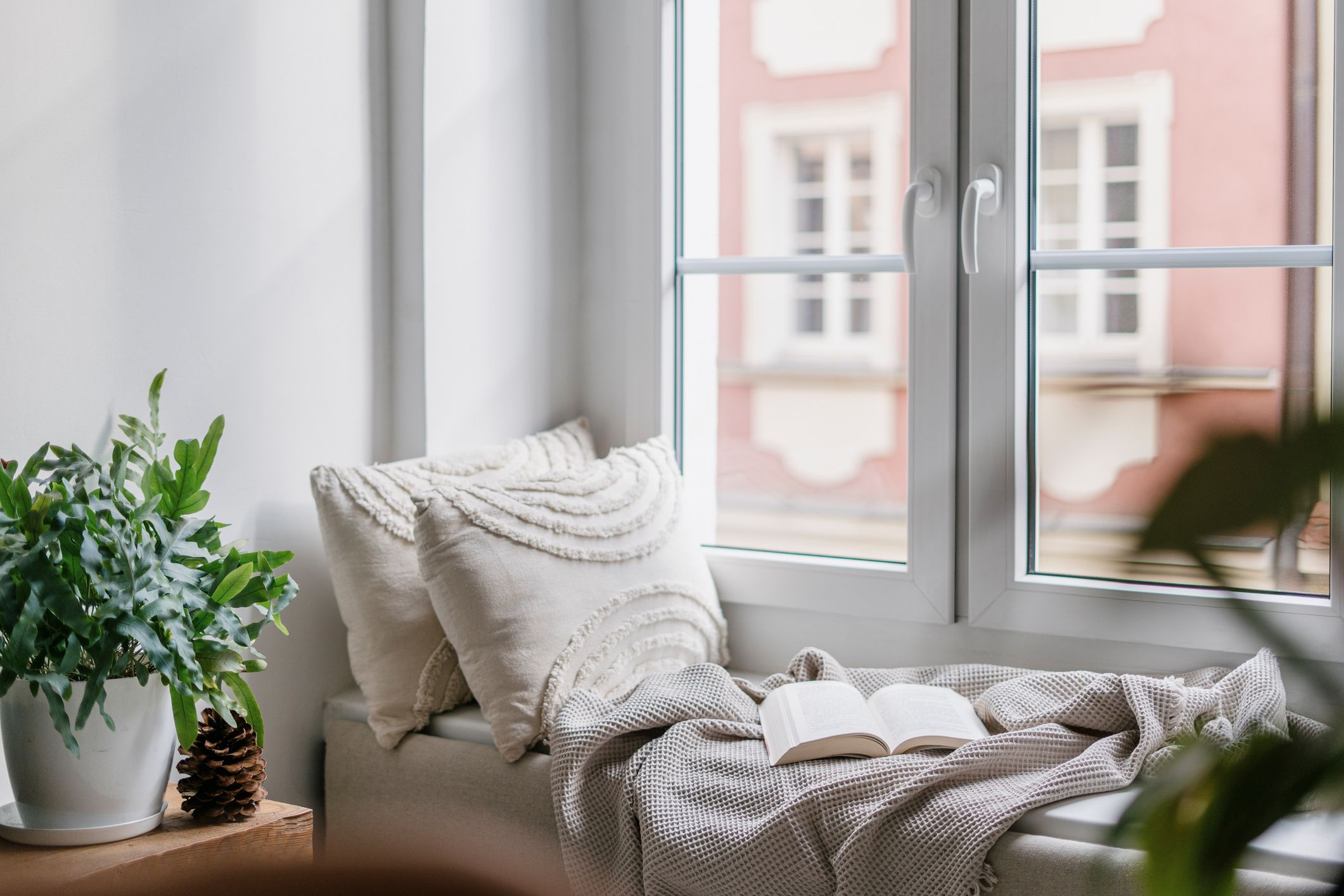 Rincón de lectura en casa con banco bajo la ventana, cojines, manta y luz natural