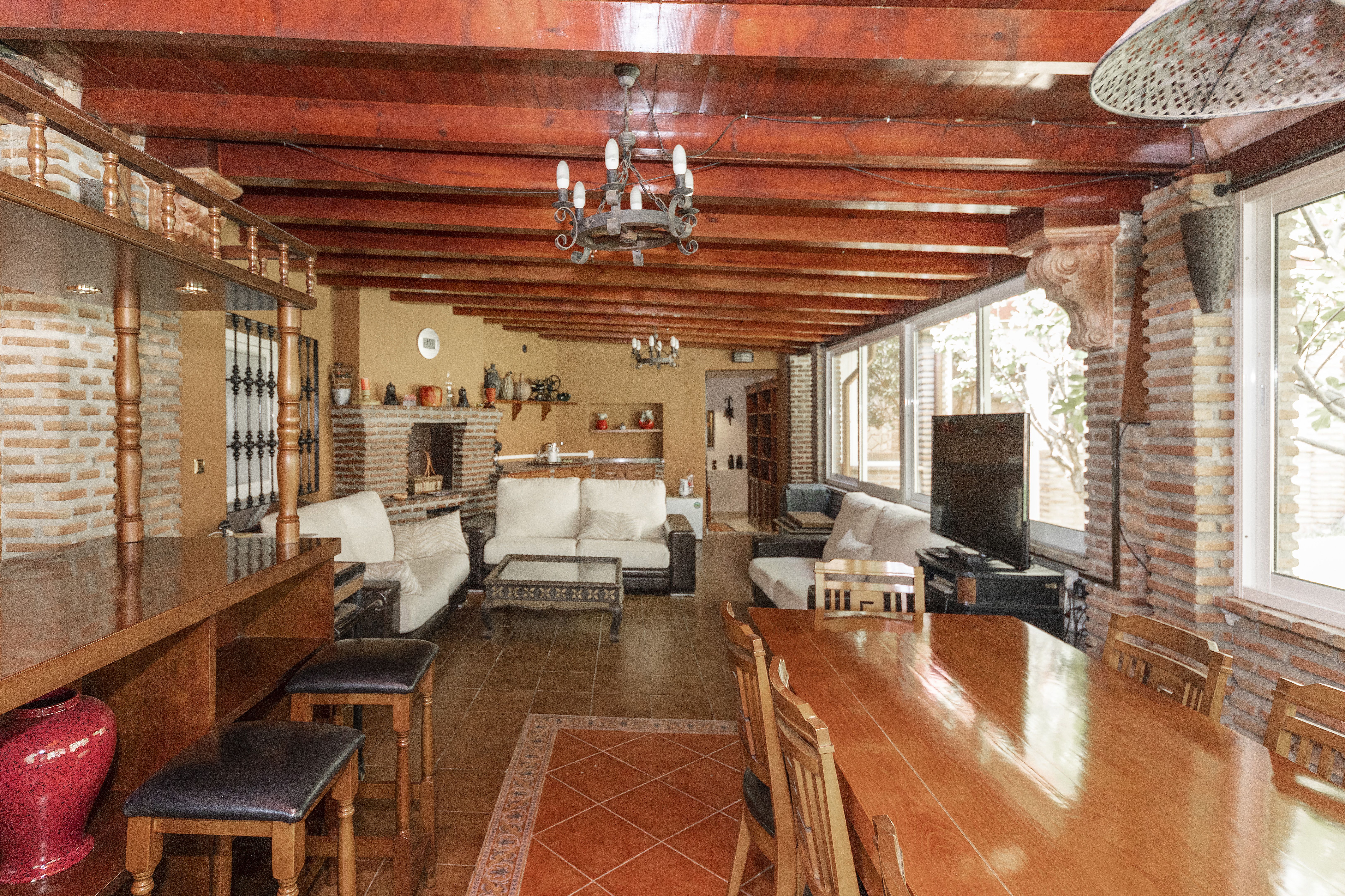Salón comedor rústico de chalet de lujo en Málaga con mesa grande, barra, vigas de madera y zona de estar