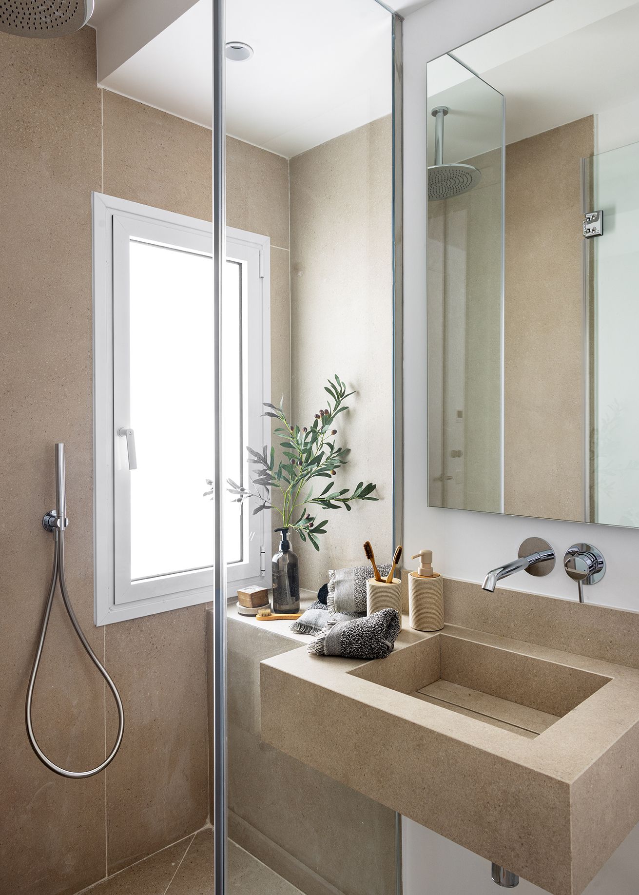 Baño minimalista con ducha de obra, lavabo integrado y acabados en tonos piedra, diseñado para aumentar el valor percibido de una vivienda mediante una estética elegante y atemporal.