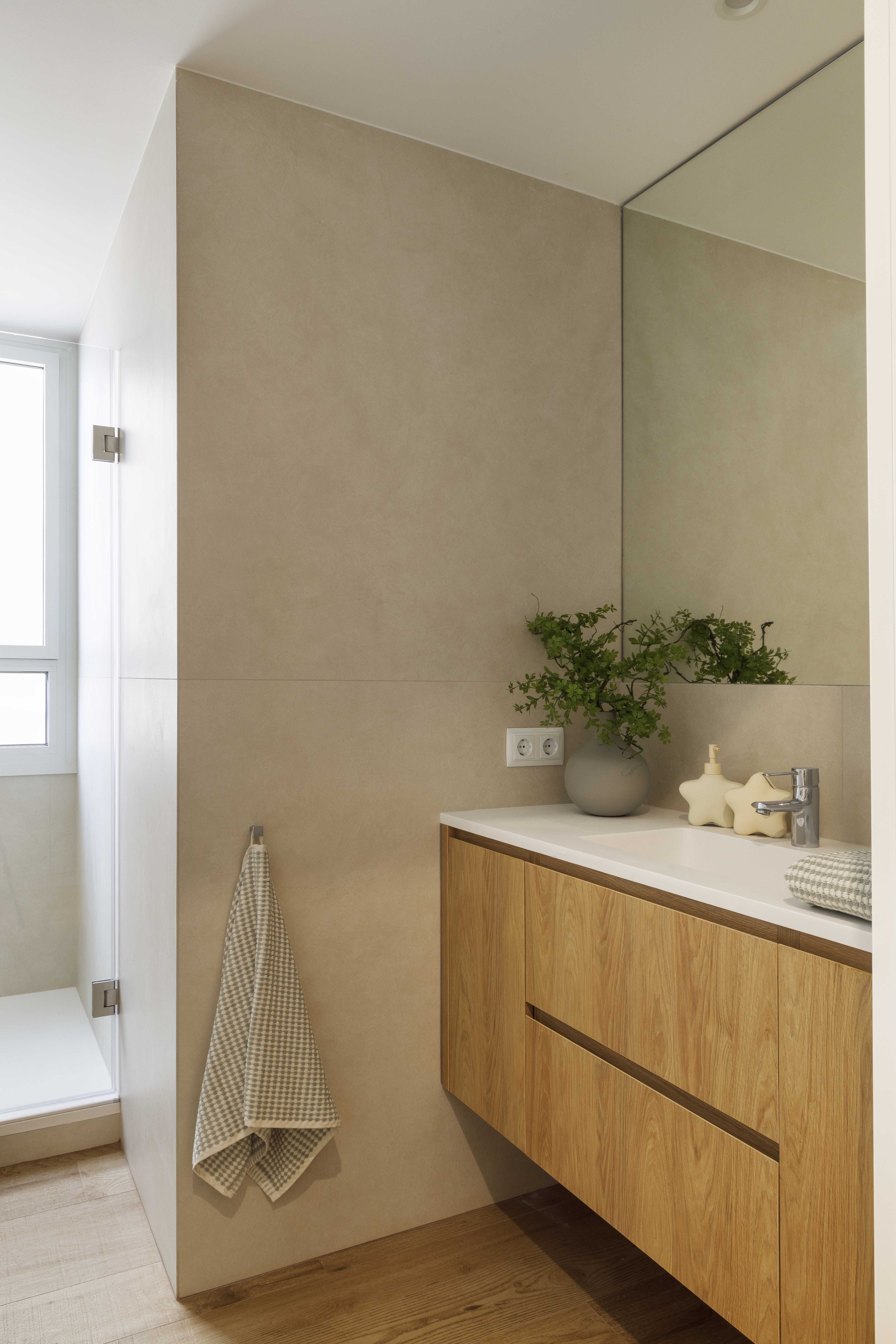 Baño moderno con mueble suspendido de madera, lavabo blanco y revestimiento en tonos beige
