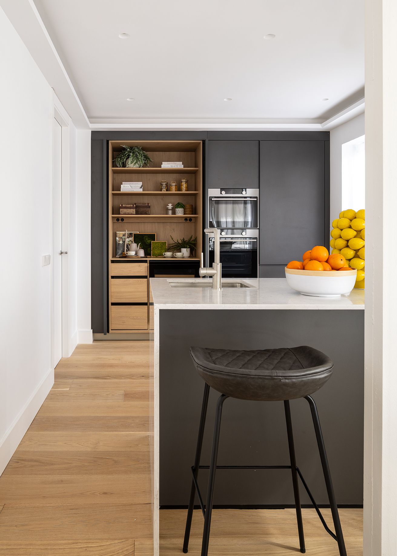 Cocina moderna con isla central, mobiliario oscuro y detalles en madera en una vivienda de Chamberí, diseñada para aumentar el valor percibido de una vivienda mediante interiorismo contemporáneo