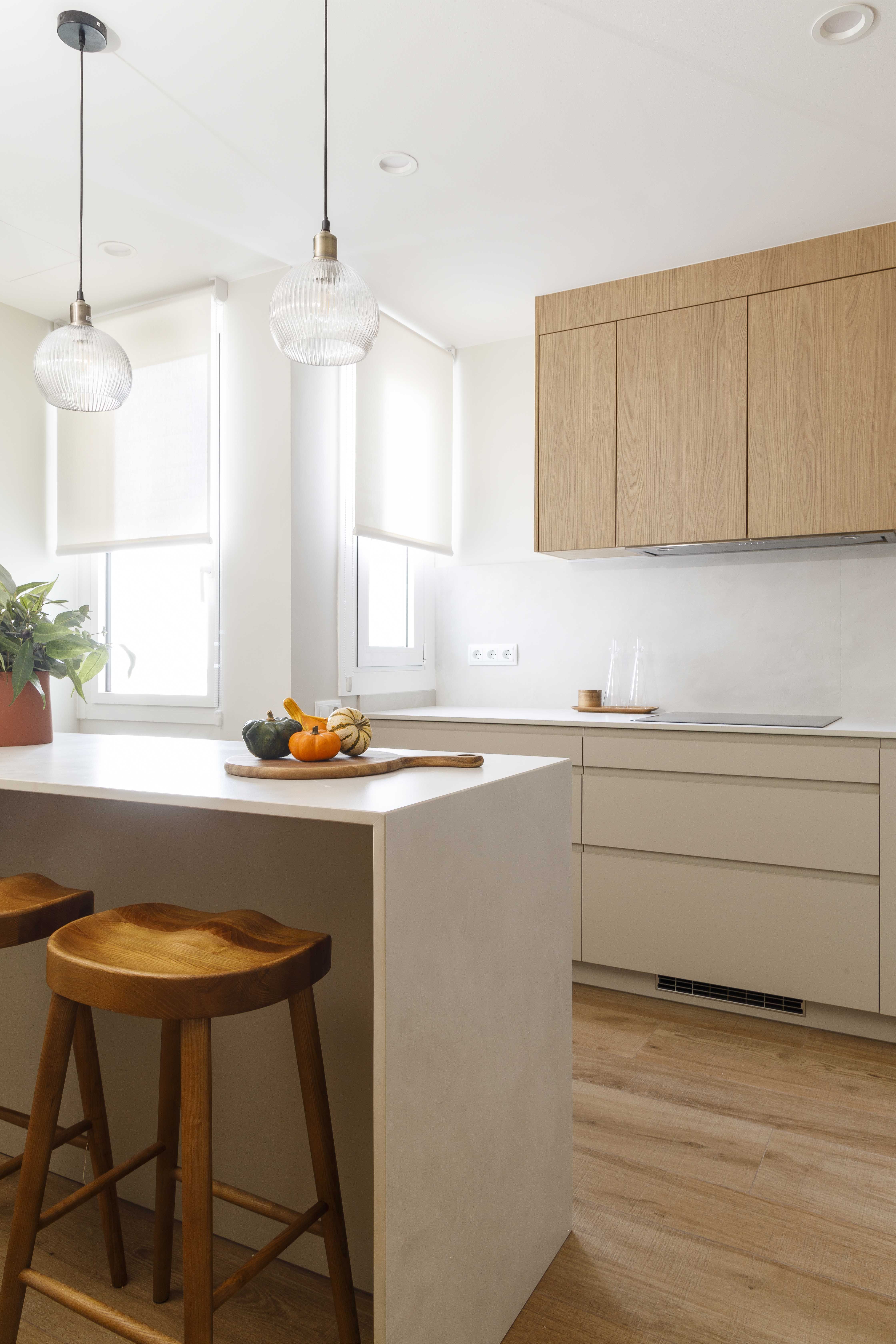 Cocina con isla y taburetes de madera en una vivienda familiar reformada y luminosa