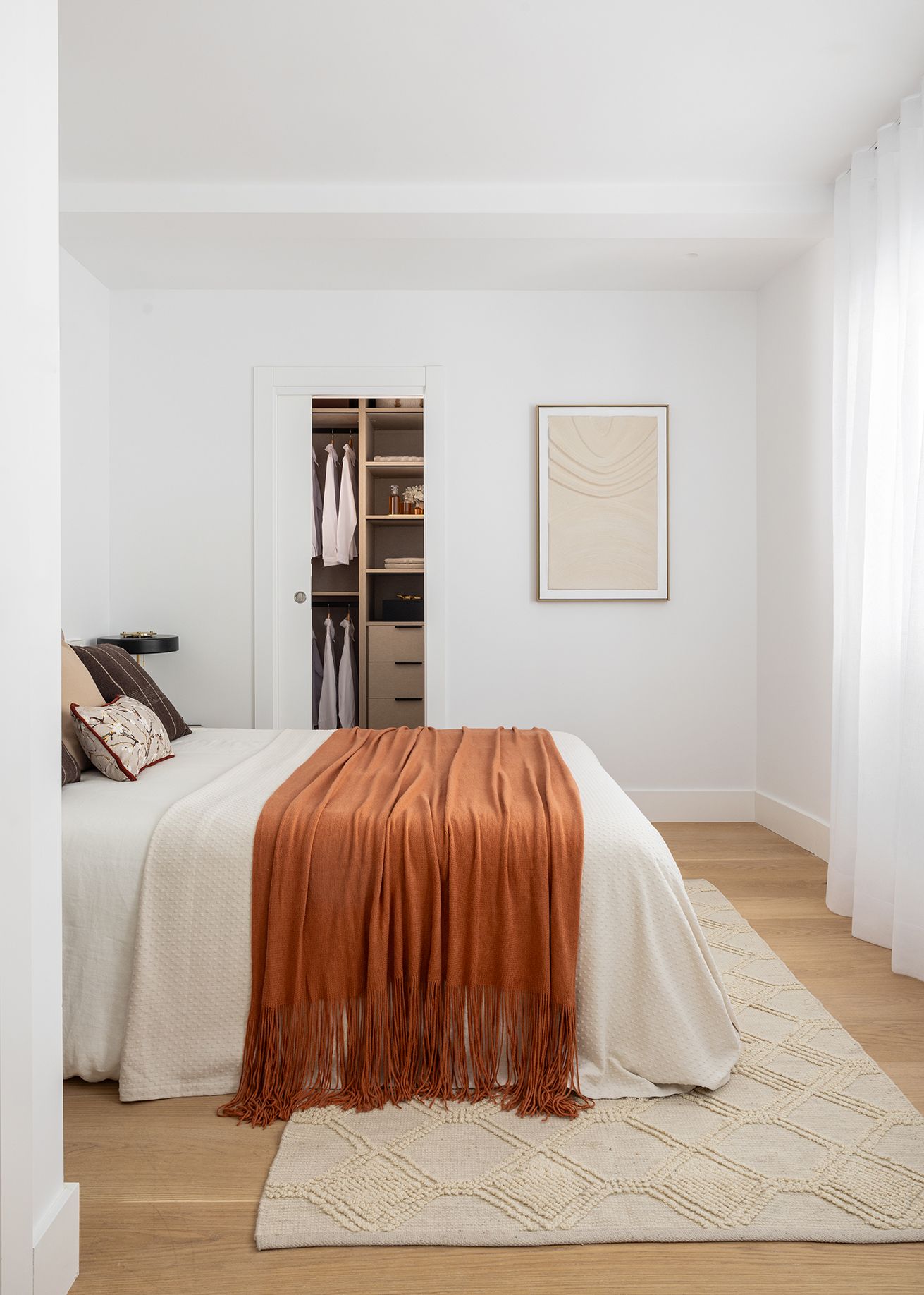 Dormitorio con vestidor abierto, decoración en tonos neutros y manta color teja, diseñado para aumentar el valor percibido de una vivienda mediante confort, orden y funcionalidad.
