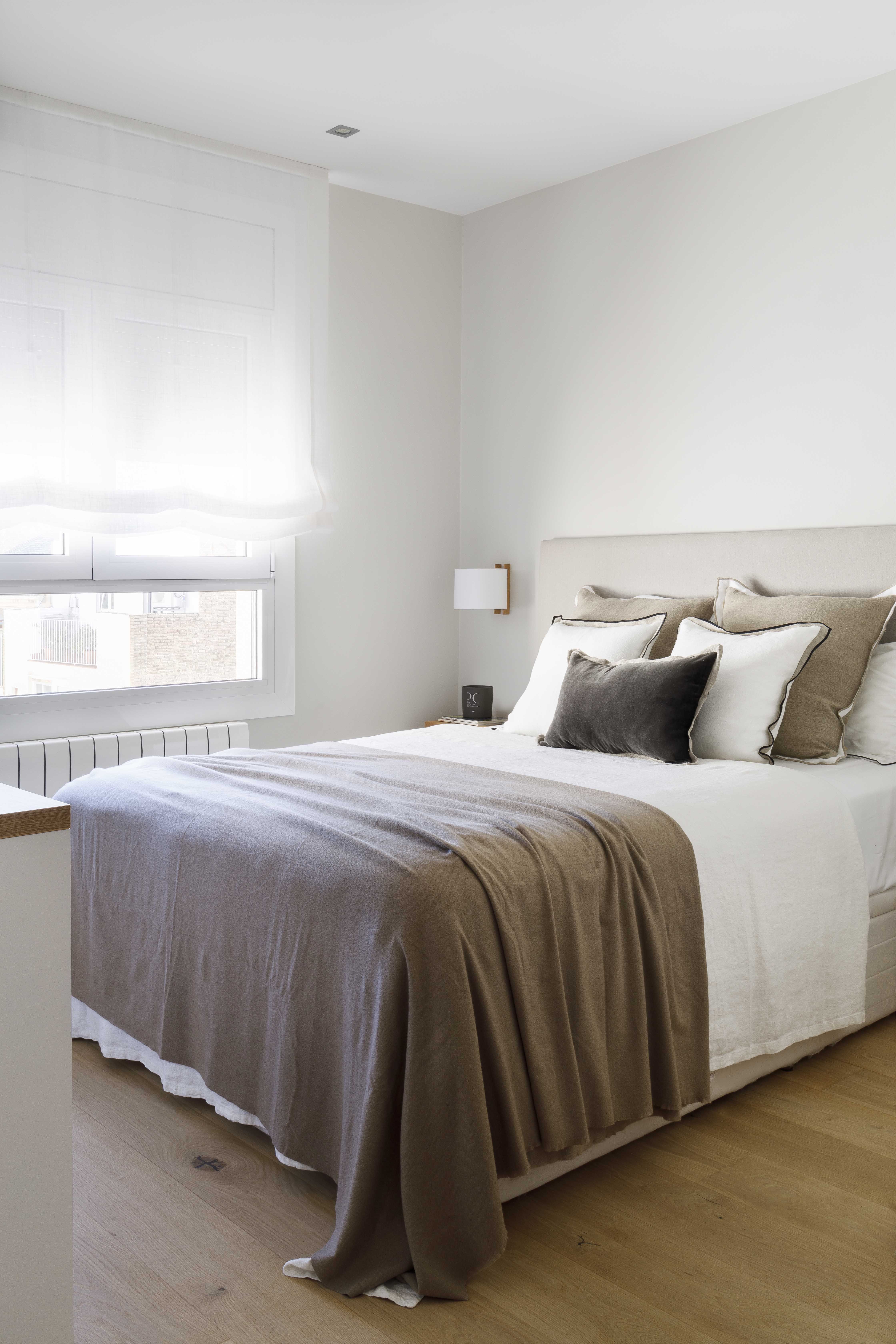 Dormitorio principal con cama tapizada y decoración en tonos beige y blanco en una vivienda familiar reformada