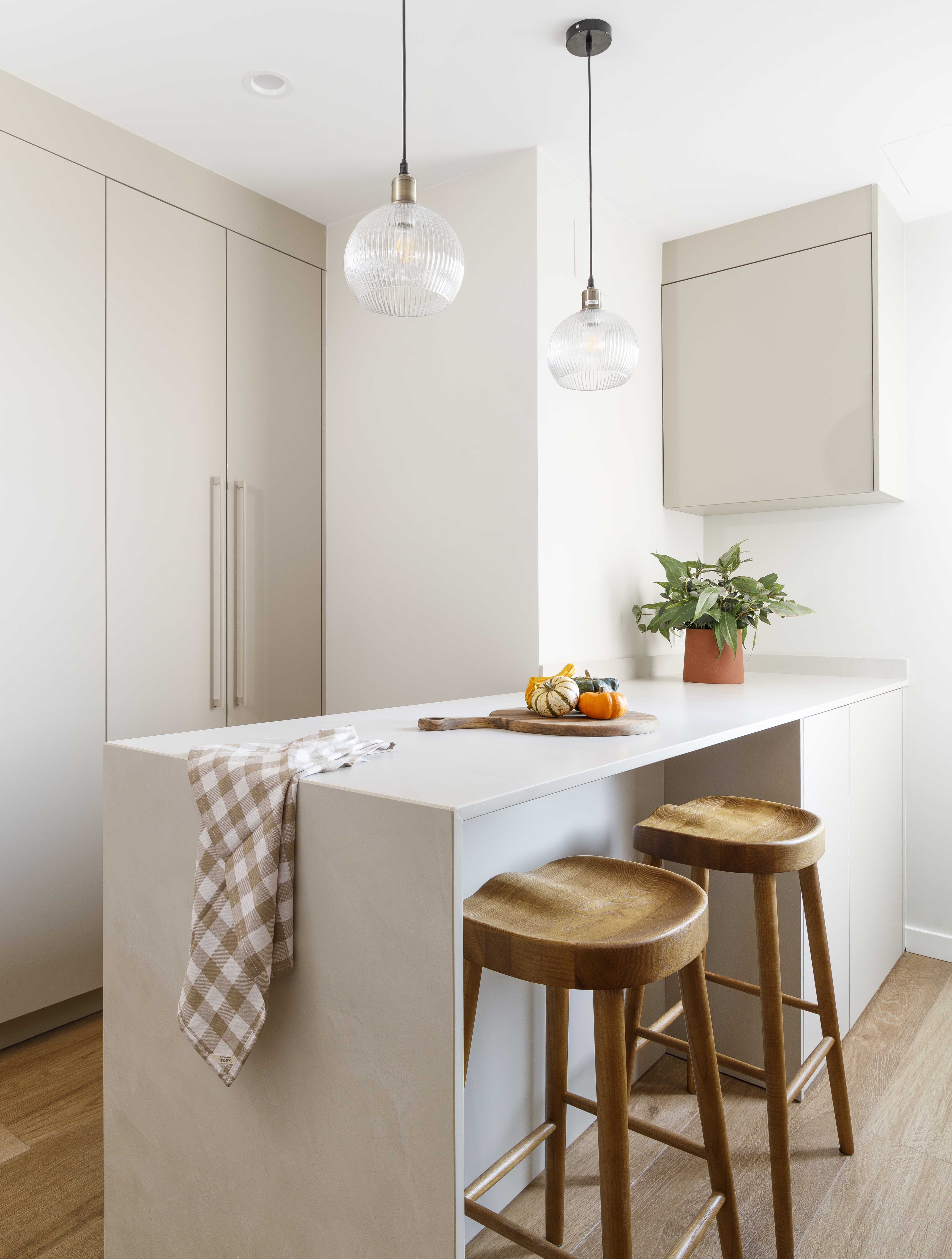 Isla de cocina minimalista con taburetes de madera en una vivienda reformada y luminosa