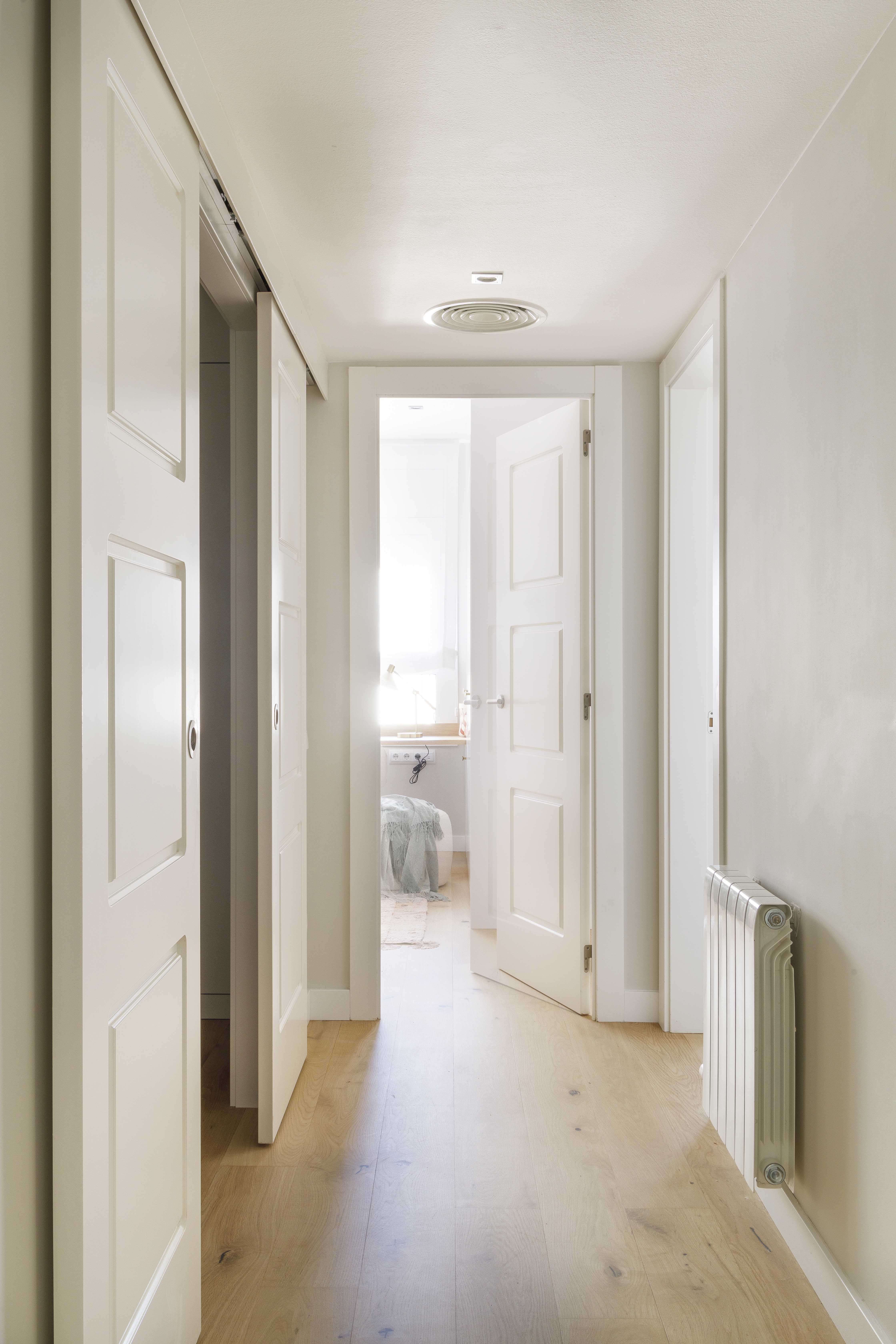 Pasillo luminoso con armarios correderos y suelo de roble natural en una vivienda reformada