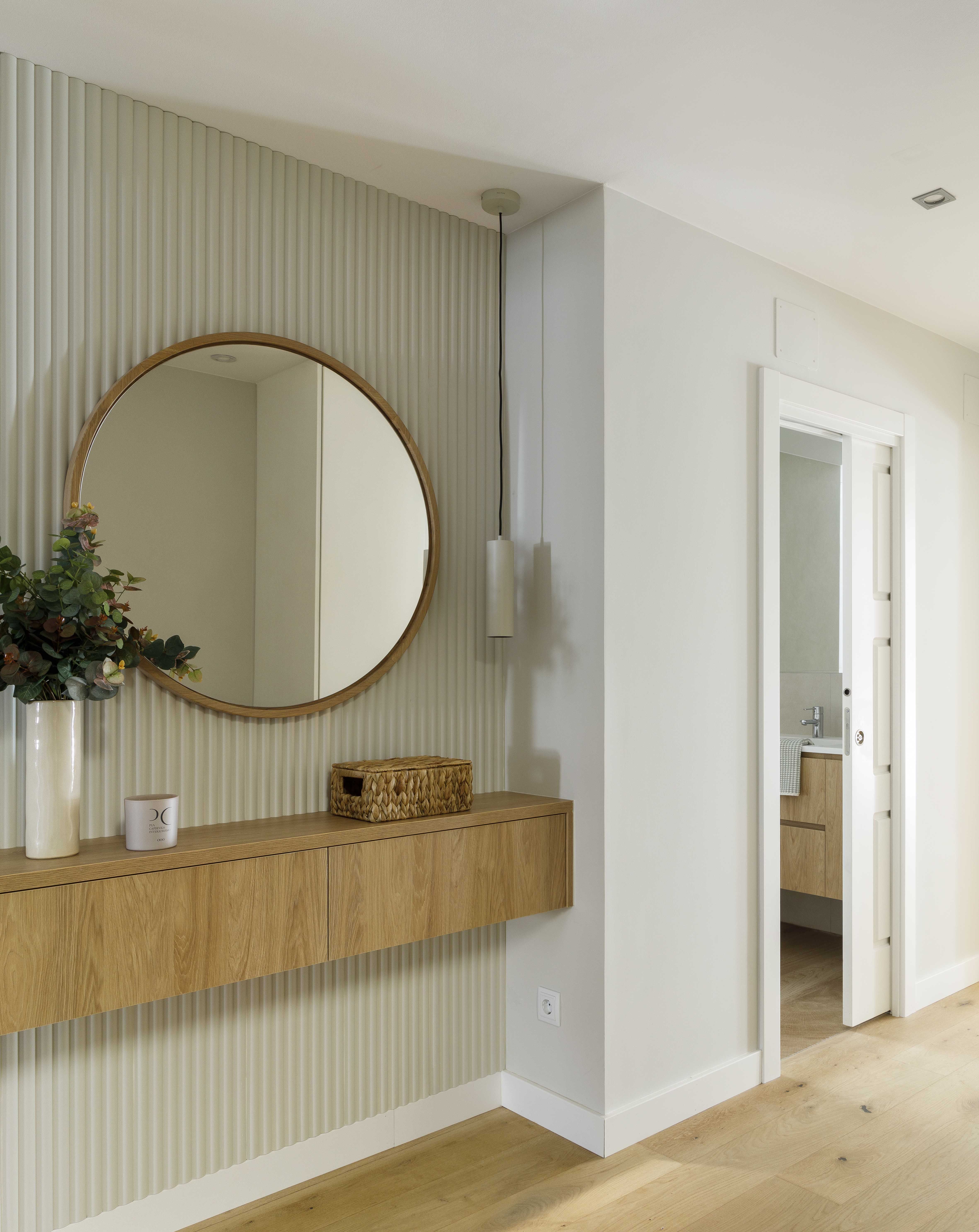 Recibidor moderno con mueble suspendido de madera y espejo redondo en una vivienda reformada