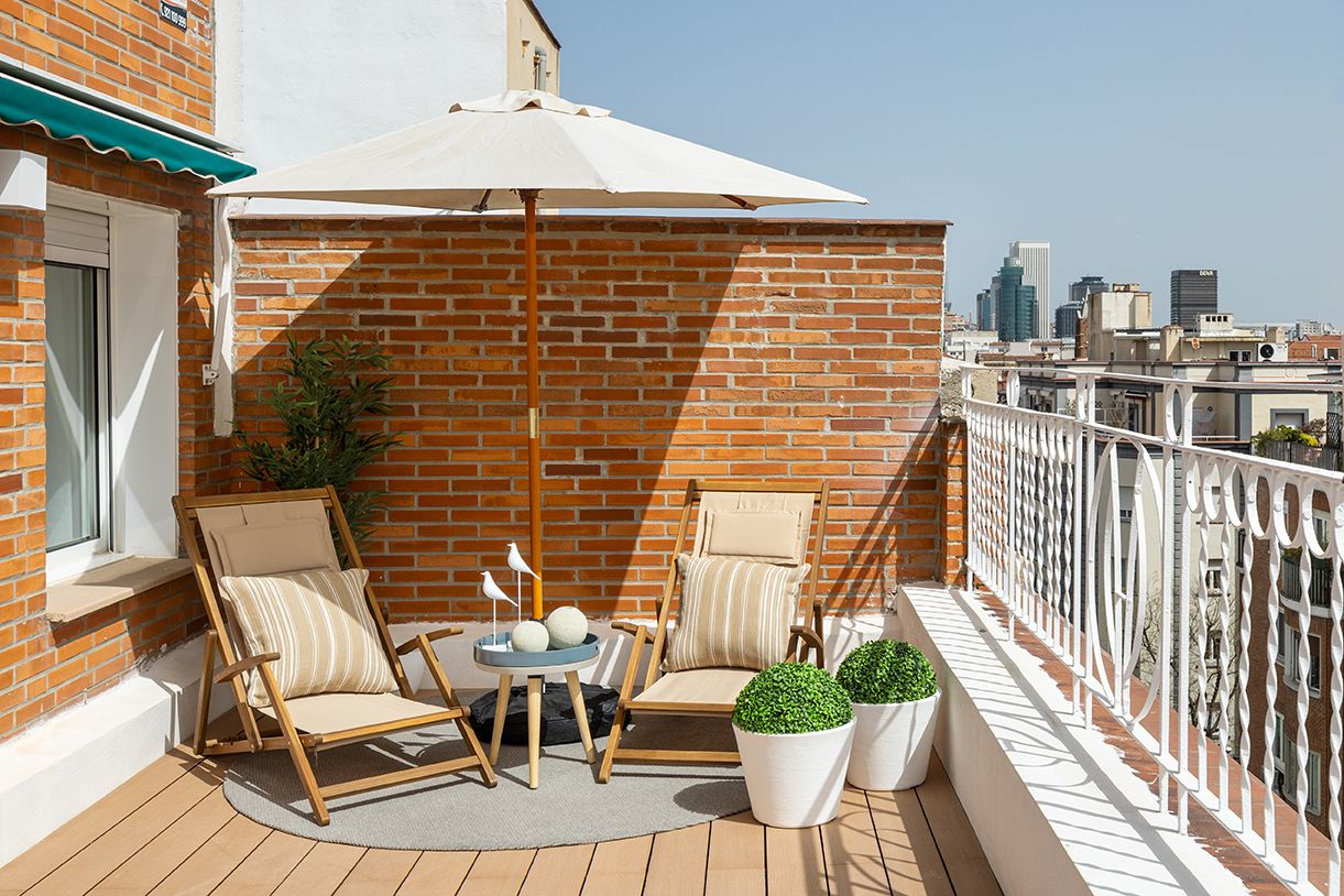 Rincón de descanso en una terraza urbana de Madrid con tumbonas, sombrilla y vistas a la ciudad, diseñado para aumentar el valor percibido de una vivienda.