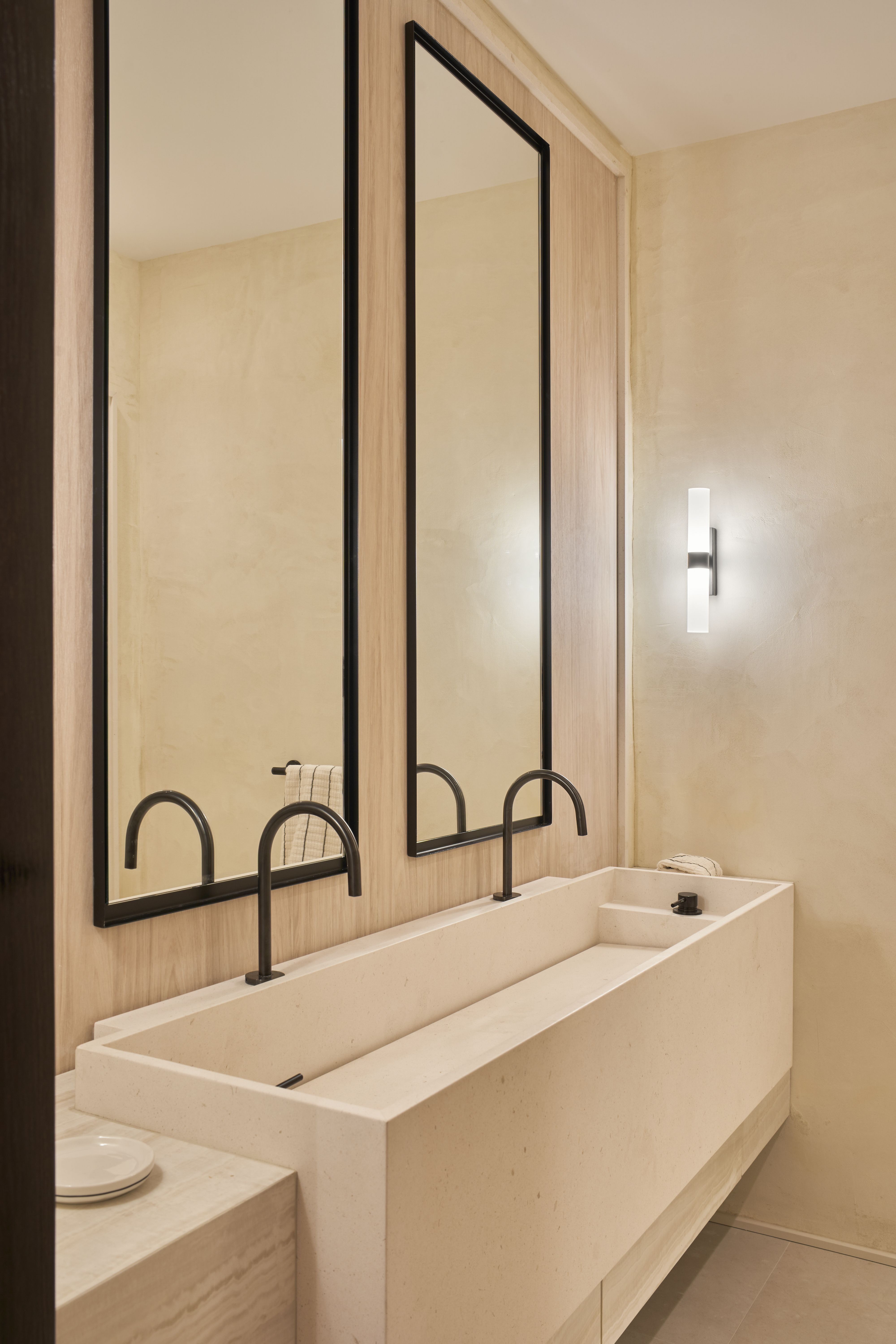 Baño de diseño con doble lavabo de piedra, espejos verticales y grifería negra en tonos naturales.