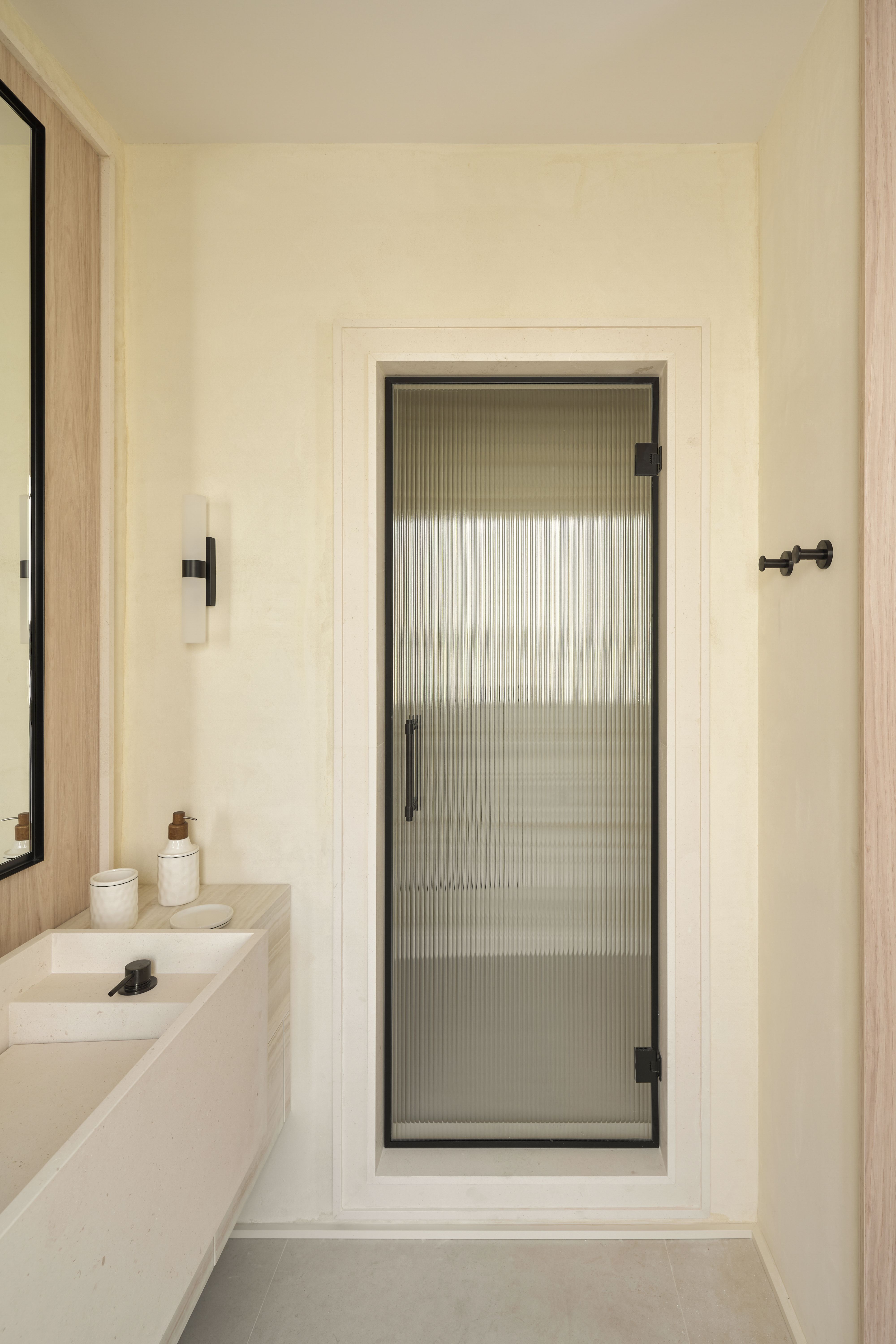 Baño contemporáneo con puerta de vidrio acanalado, lavabo suspendido y acabados en piedra y madera.
