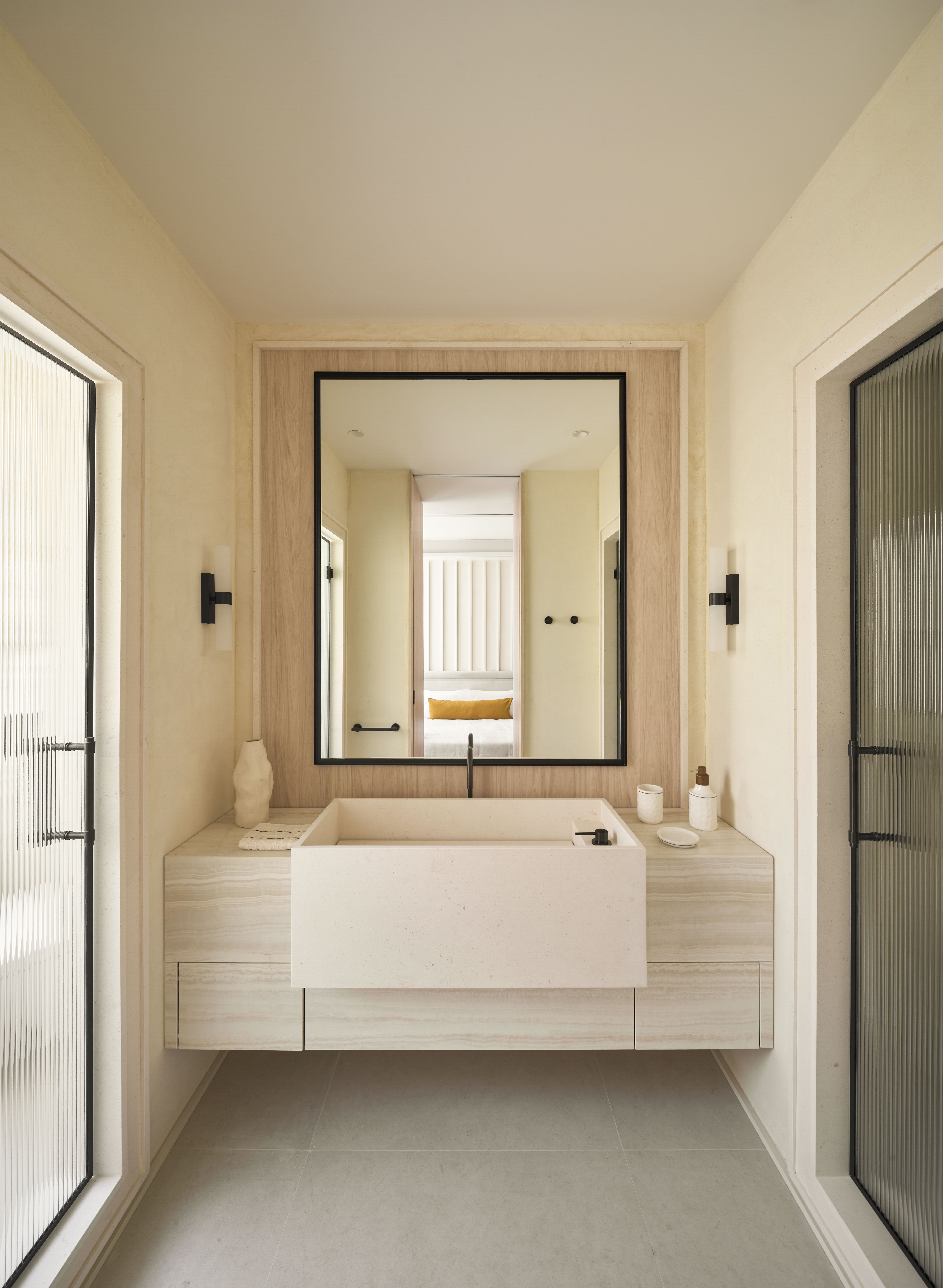 Baño de diseño con lavabo de piedra, mueble suspendido y materiales naturales en tonos cálidos.
