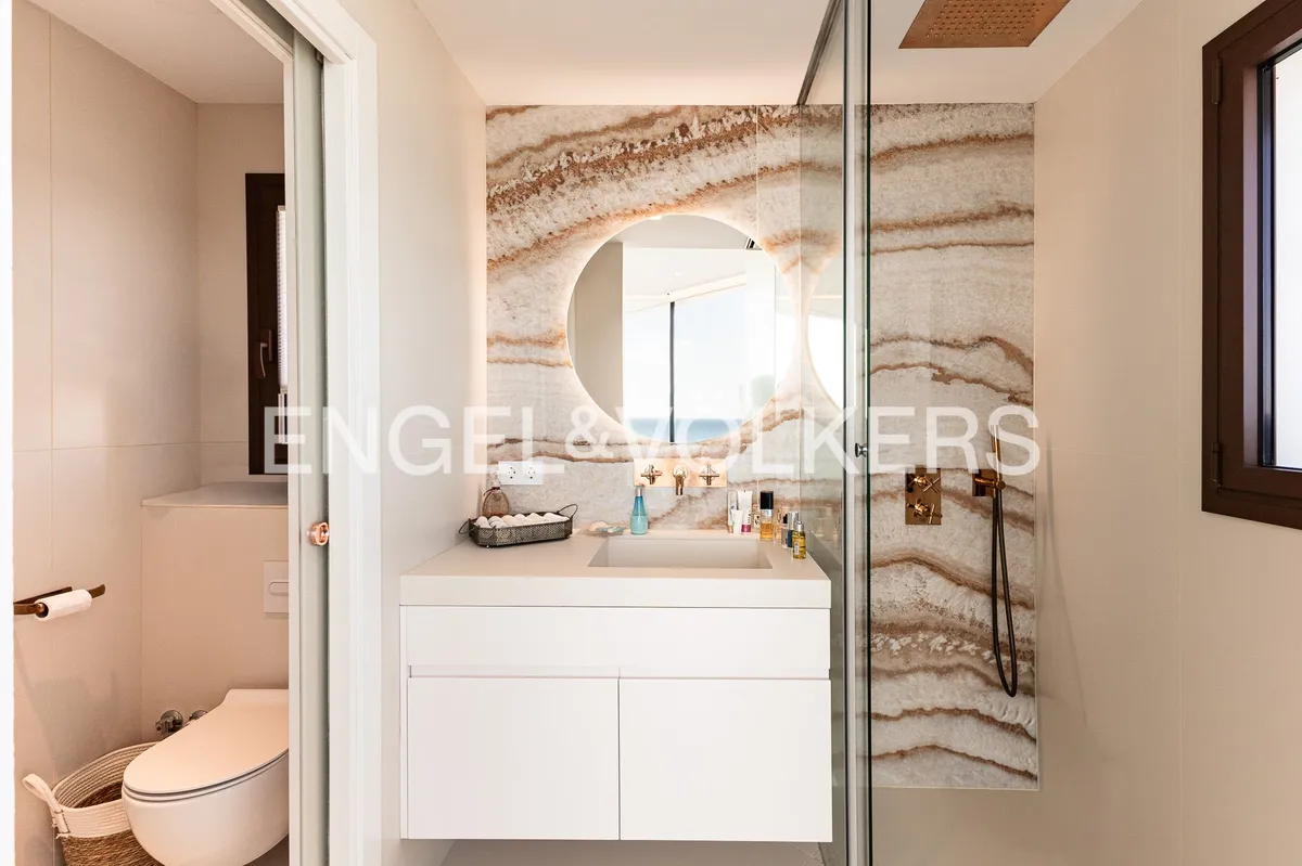 Baño de una casa en Sant Pol de Mar con revestimiento efecto piedra natural, ducha acristalada y lavabo suspendido.