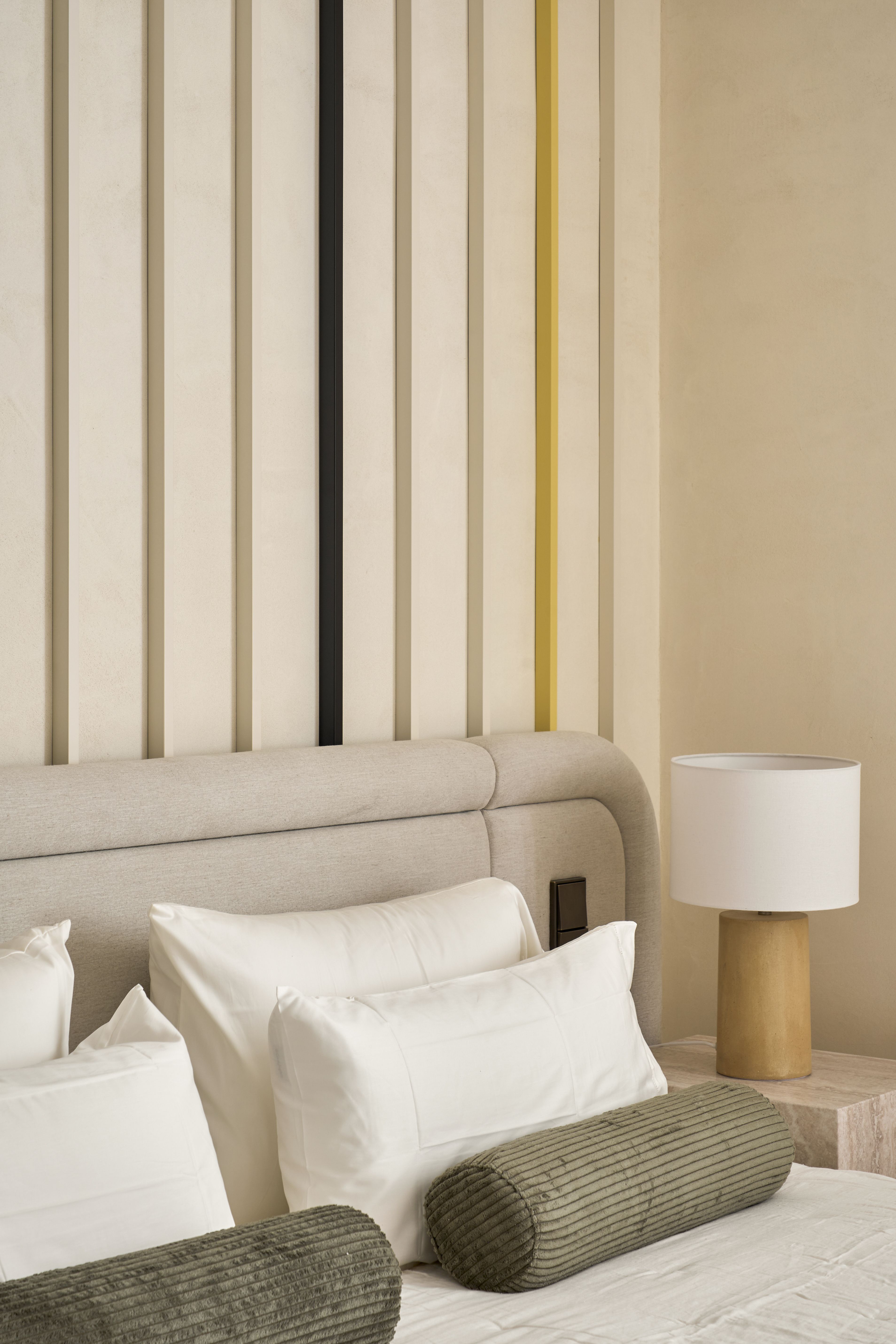 Cabecero tapizado de gran formato con panelado vertical y ropa de cama en tonos neutros en un dormitorio elegante.