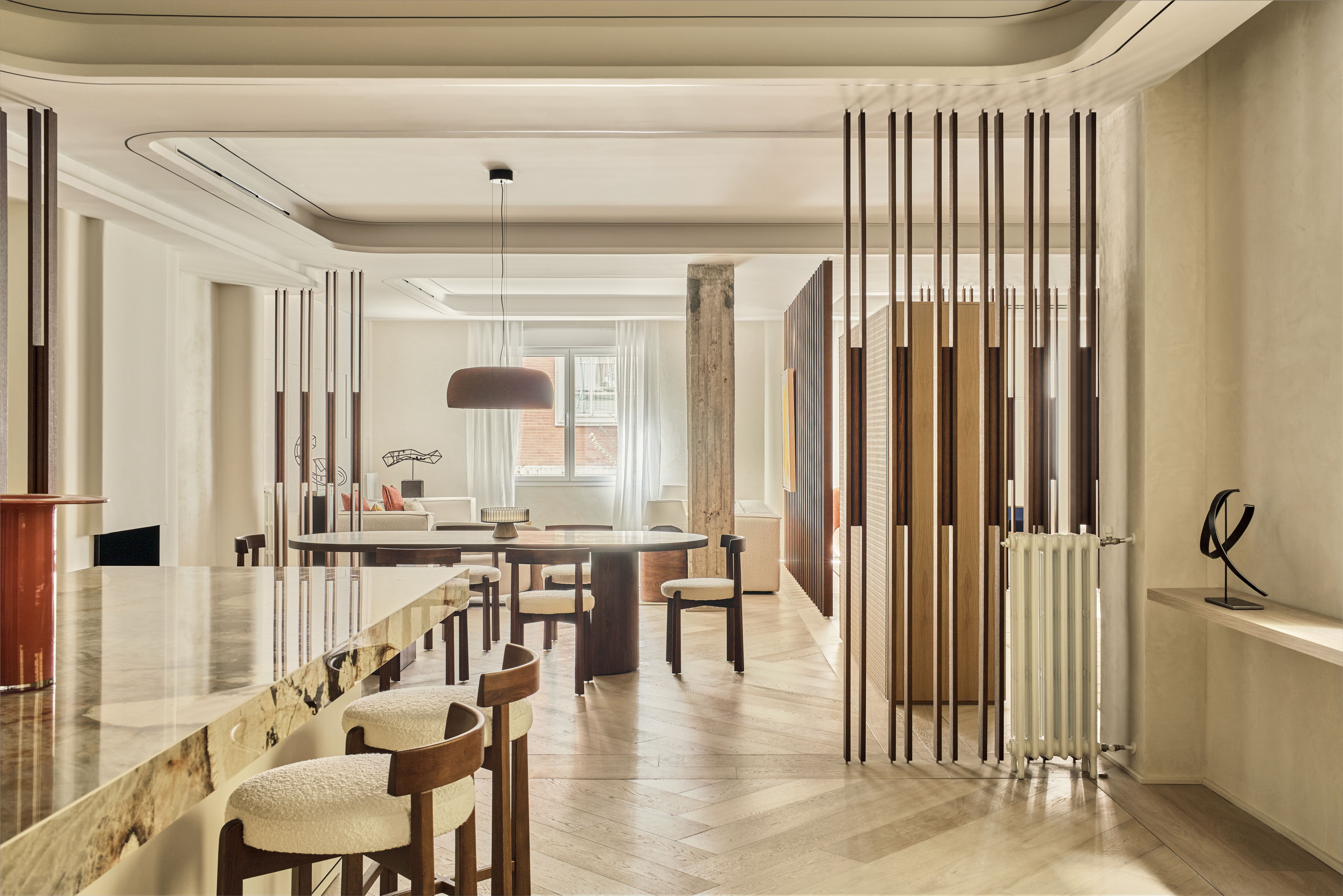 Cocina abierta al comedor con celosías de madera, suelo continuo y materiales naturales en una reforma de diseño contemporáneo.