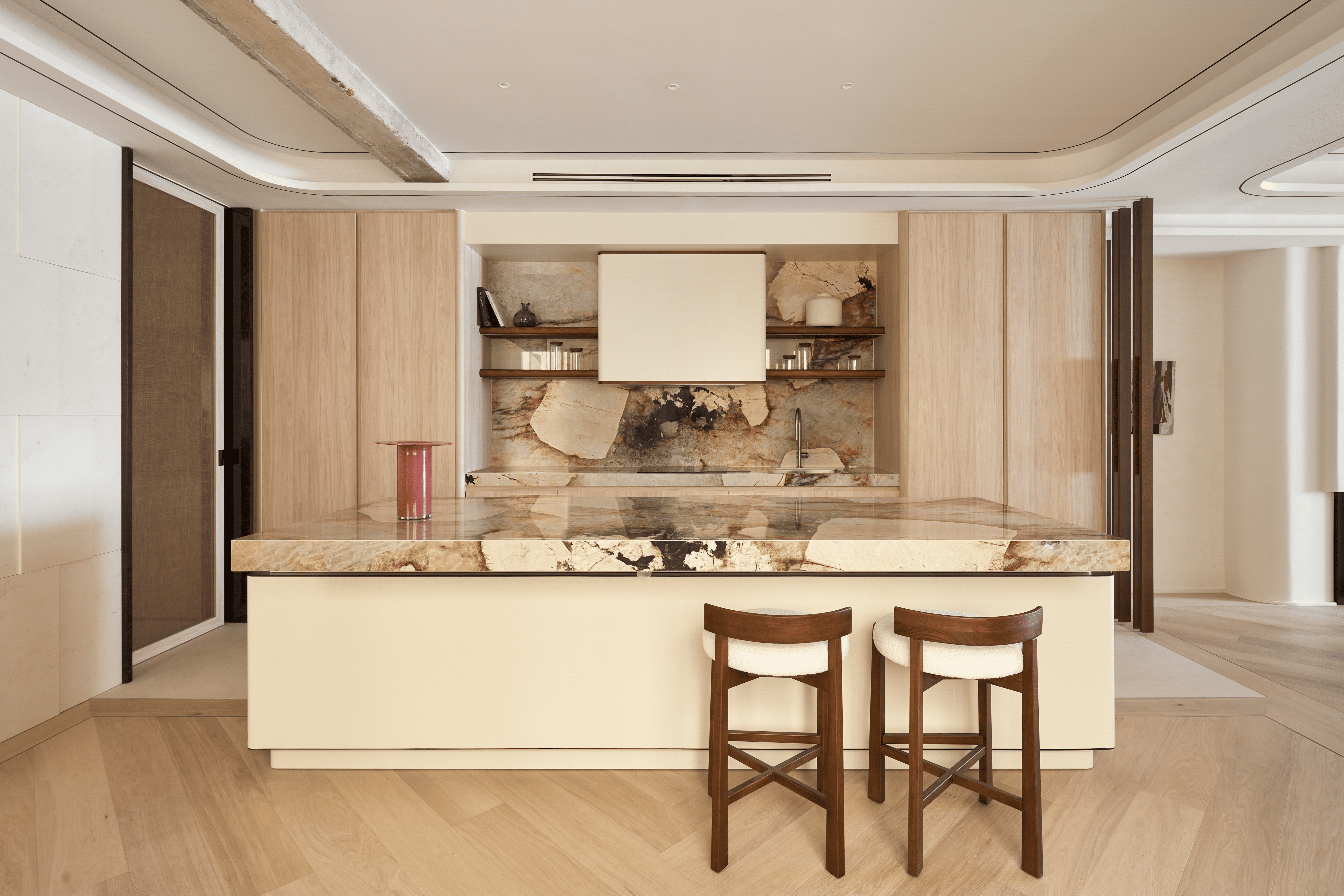 Cocina con isla de piedra natural de gran formato y mobiliario de madera clara.