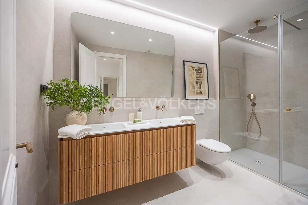 Baño principal de una casa con terraza junto a El Retiro con mueble de madera acanalada, ducha a ras de suelo y acabados en tonos piedra