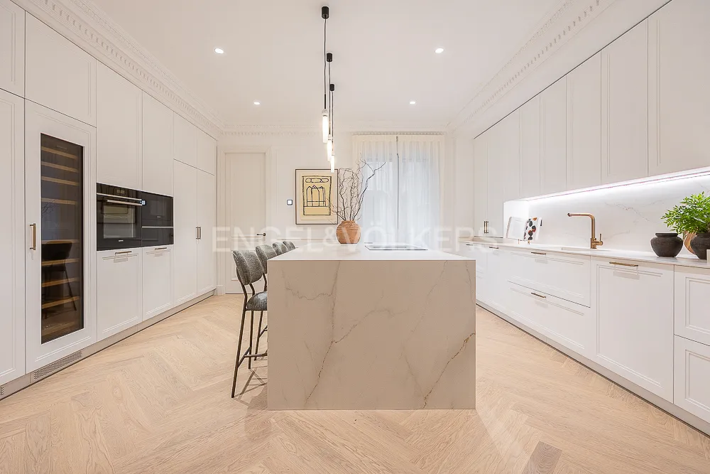 Cocina con isla central de una casa con terraza junto a El Retiro en Recoletos, Madrid, con mobiliario blanco y encimera efecto mármol