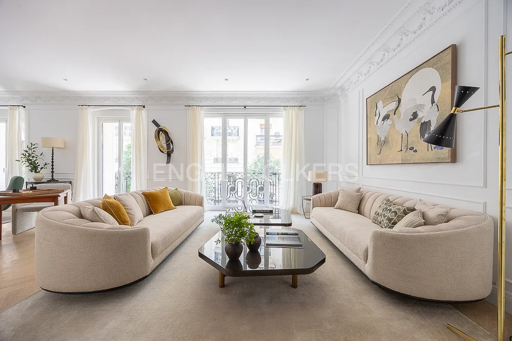 Salón principal de una casa con terraza junto a El Retiro con sofás curvos, molduras clásicas y grandes ventanales